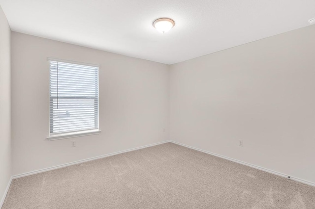 spare room featuring light colored carpet and baseboards