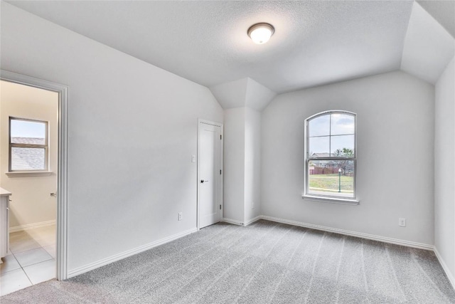 unfurnished room featuring lofted ceiling, a textured ceiling, baseboards, and light colored carpet