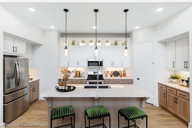 kitchen with light stone countertops, appliances with stainless steel finishes, a center island with sink, light hardwood / wood-style flooring, and white cabinets