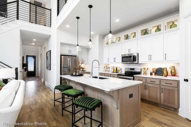 kitchen with white cabinets, sink, an island with sink, appliances with stainless steel finishes, and light stone counters