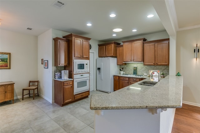 kitchen with white appliances, a kitchen breakfast bar, sink, light stone countertops, and kitchen peninsula