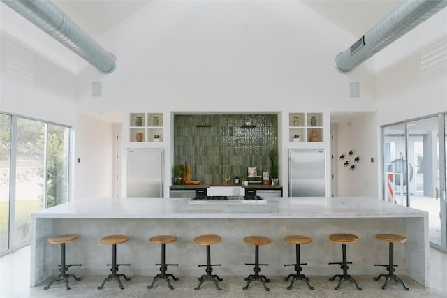 kitchen featuring stainless steel built in refrigerator, stainless steel fridge, a towering ceiling, and a breakfast bar area