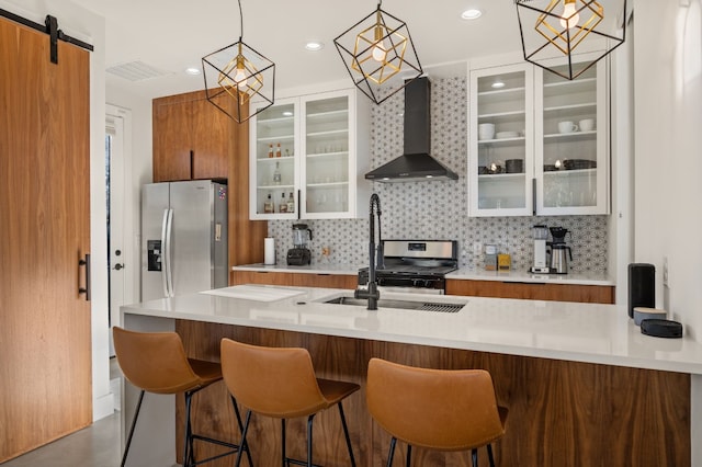 kitchen with backsplash, stainless steel appliances, sink, wall chimney range hood, and a barn door