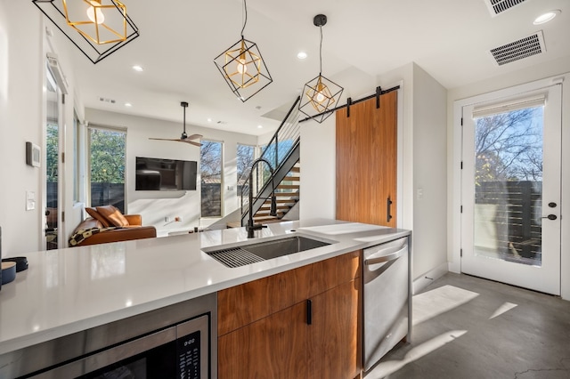 kitchen with pendant lighting, stainless steel dishwasher, a barn door, built in microwave, and plenty of natural light