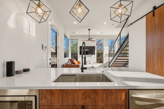 kitchen with dishwasher, sink, hanging light fixtures, ceiling fan, and a barn door