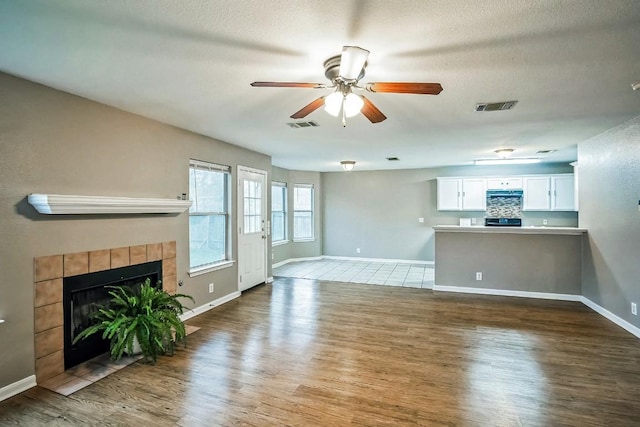 unfurnished living room with a tiled fireplace, ceiling fan, hardwood / wood-style floors, and a textured ceiling