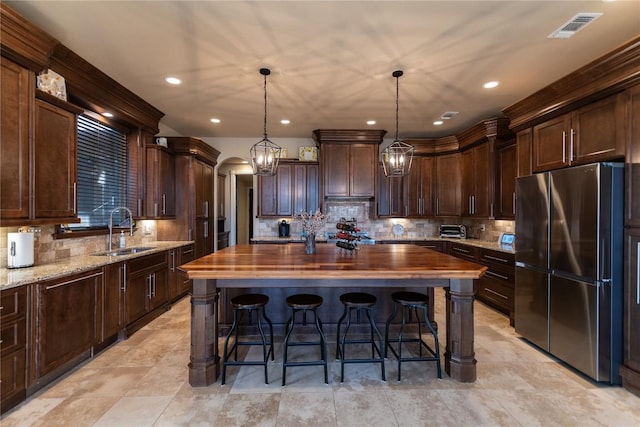 kitchen featuring arched walkways, a center island, hanging light fixtures, freestanding refrigerator, and a sink