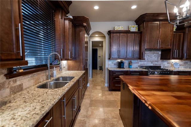 kitchen with backsplash, wooden counters, range with gas cooktop, arched walkways, and a sink