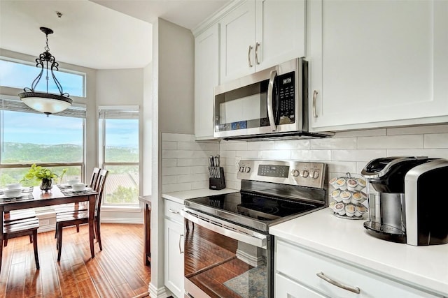 kitchen with decorative backsplash, appliances with stainless steel finishes, wood-type flooring, white cabinets, and hanging light fixtures