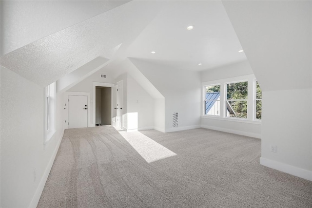 additional living space featuring light colored carpet, lofted ceiling, and a textured ceiling