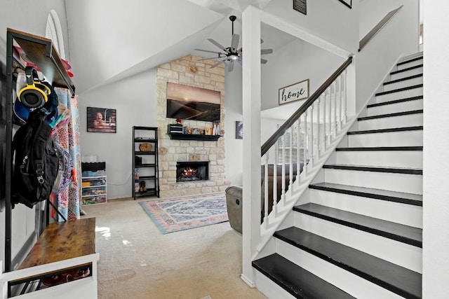 interior space featuring carpet flooring, ceiling fan, a stone fireplace, and high vaulted ceiling