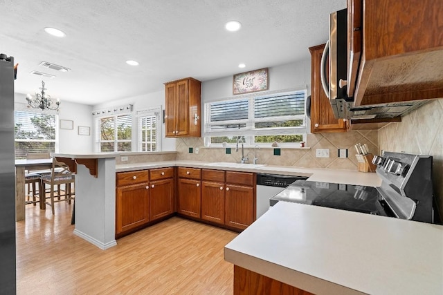 kitchen with an inviting chandelier, sink, light hardwood / wood-style flooring, kitchen peninsula, and stainless steel appliances