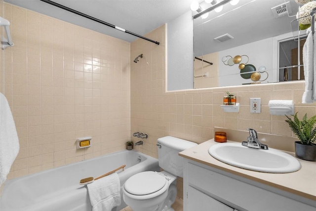 full bathroom with tiled shower / bath combo, tasteful backsplash, toilet, vanity, and tile walls