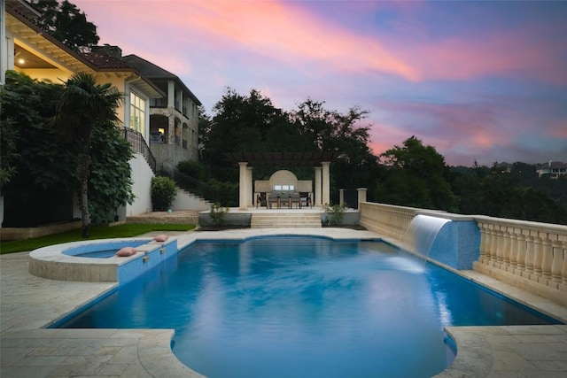 pool at dusk featuring an in ground hot tub and pool water feature