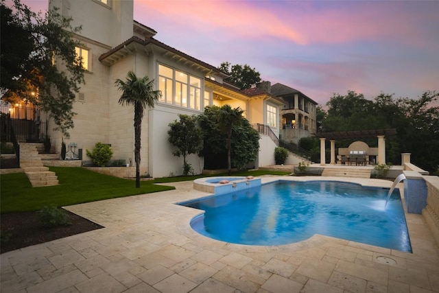 pool at dusk featuring an in ground hot tub, a yard, pool water feature, and a patio