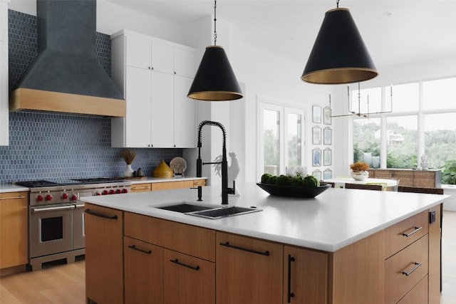 kitchen featuring designer range, custom range hood, sink, decorative light fixtures, and white cabinets