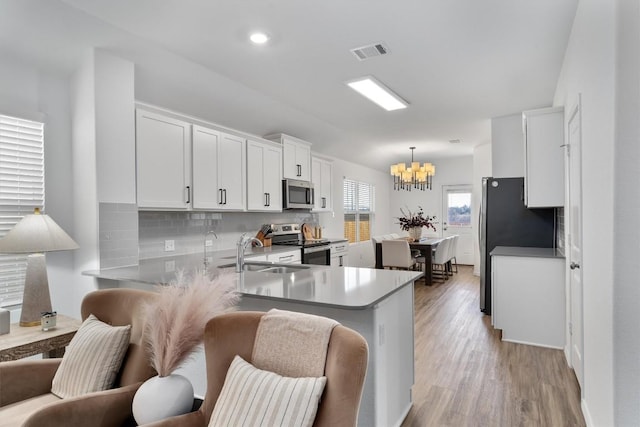 kitchen with hanging light fixtures, stainless steel appliances, tasteful backsplash, kitchen peninsula, and white cabinets