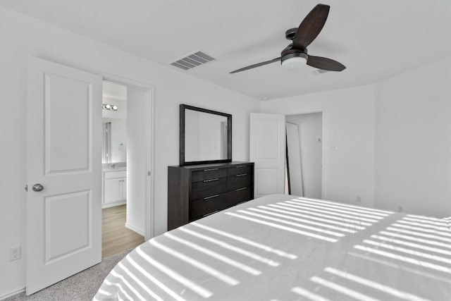 bedroom with ceiling fan, light colored carpet, and connected bathroom