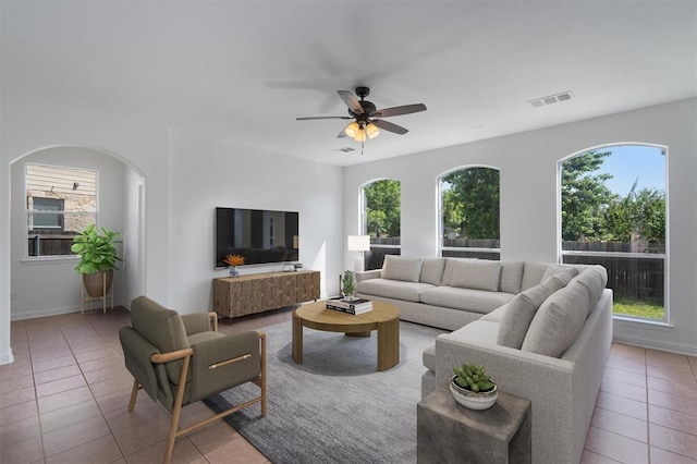 living area with a ceiling fan, arched walkways, baseboards, tile patterned flooring, and visible vents