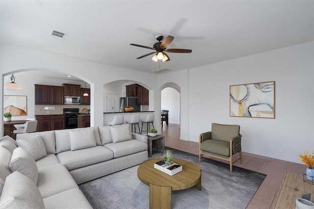 living room featuring arched walkways, visible vents, tile patterned floors, and ceiling fan