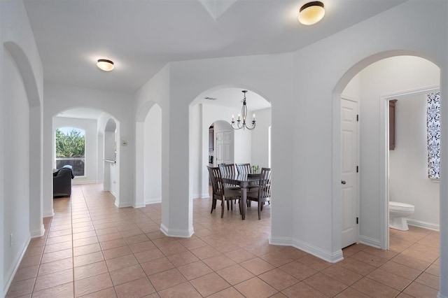 corridor featuring light tile patterned floors and an inviting chandelier