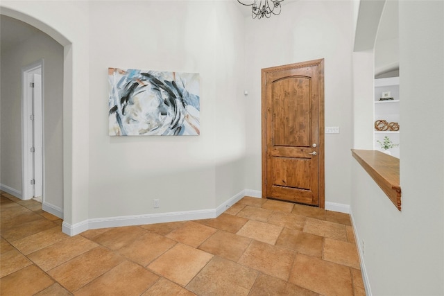 hallway with built in shelves, arched walkways, stone finish floor, and baseboards