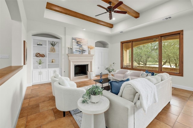 living room with a fireplace with raised hearth, visible vents, baseboards, built in features, and beam ceiling