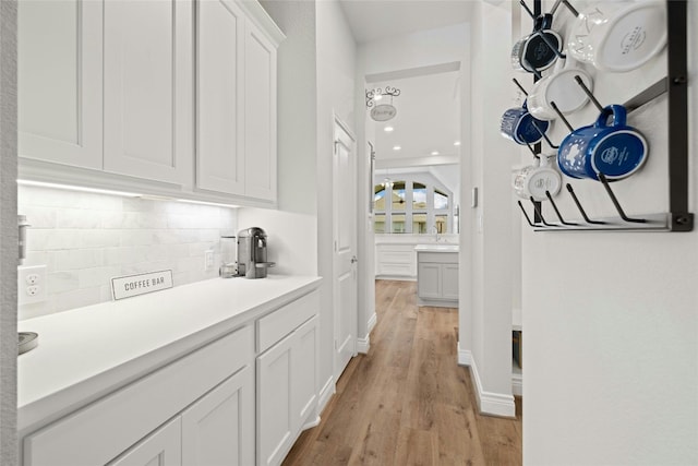 bar with white cabinets, backsplash, and light hardwood / wood-style flooring