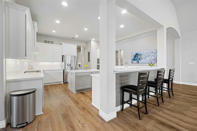 kitchen with stainless steel appliances, light hardwood / wood-style floors, decorative backsplash, and white cabinets