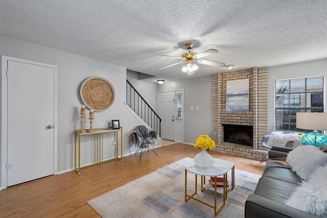 living room with ceiling fan, light hardwood / wood-style flooring, a textured ceiling, and a brick fireplace