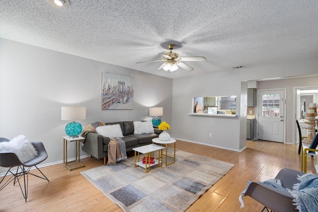 living room with a textured ceiling, light hardwood / wood-style floors, and ceiling fan