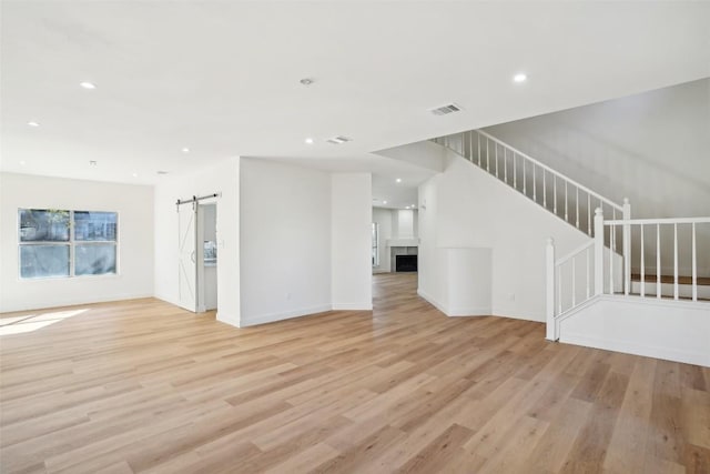 unfurnished living room with a barn door, a fireplace, visible vents, stairs, and light wood finished floors