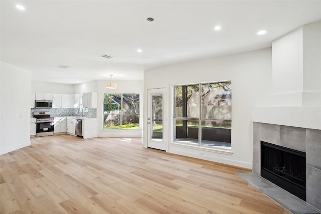 unfurnished living room featuring sink, light hardwood / wood-style floors, and a tiled fireplace