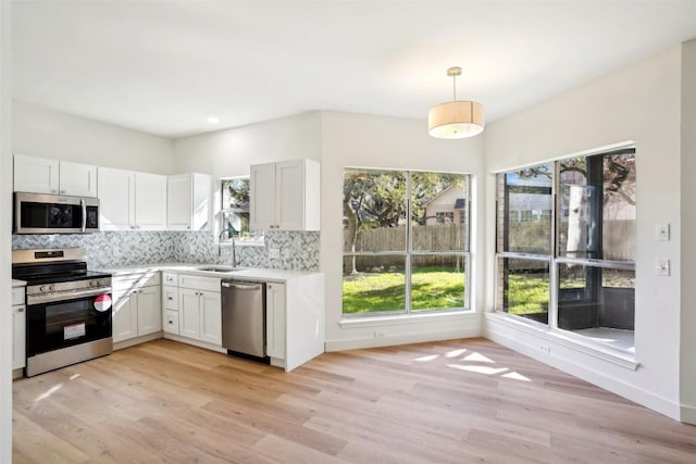 kitchen featuring white cabinets, appliances with stainless steel finishes, light wood-type flooring, and hanging light fixtures