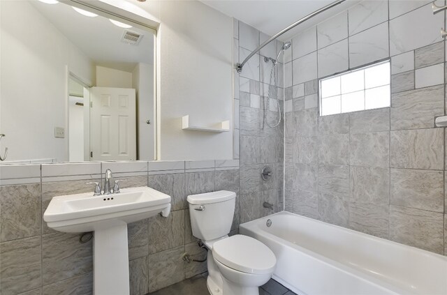 full bathroom with tiled shower / bath combo, toilet, tile walls, and sink