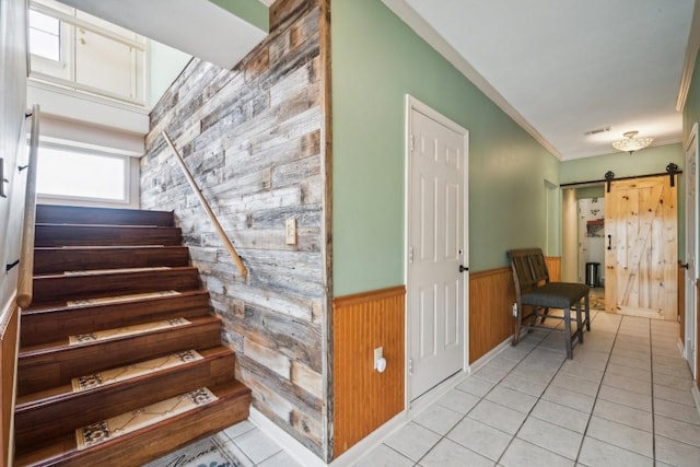 staircase with wood walls, tile patterned flooring, a barn door, and ornamental molding