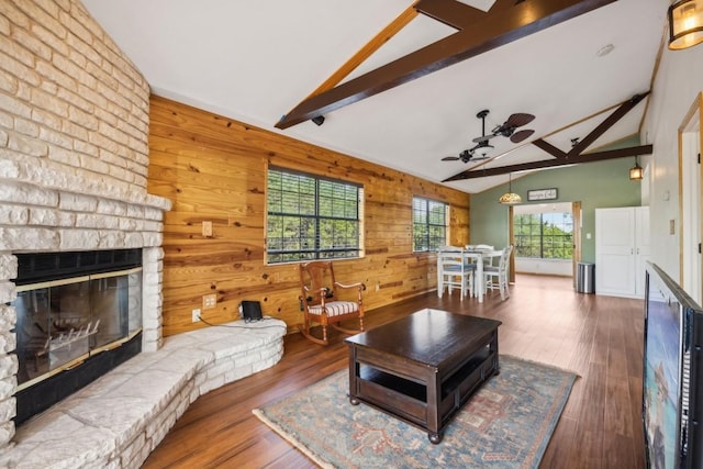 living room featuring ceiling fan, dark hardwood / wood-style flooring, lofted ceiling with beams, wood walls, and a fireplace