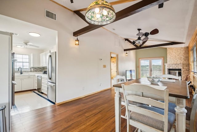 dining space with a fireplace, vaulted ceiling with beams, ceiling fan, and sink