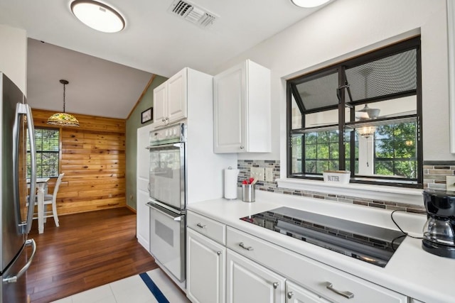 kitchen with stainless steel fridge, stovetop, vaulted ceiling, decorative light fixtures, and white cabinets