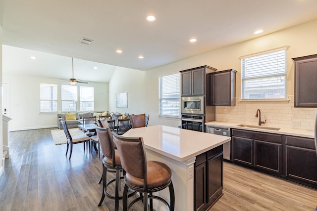 kitchen with dark brown cabinetry, stainless steel appliances, ceiling fan, sink, and a kitchen island