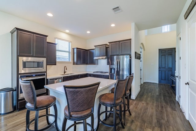 kitchen with appliances with stainless steel finishes, dark brown cabinetry, dark wood-type flooring, sink, and a kitchen island