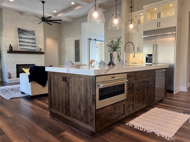 kitchen with oven, beam ceiling, dark brown cabinetry, and an island with sink