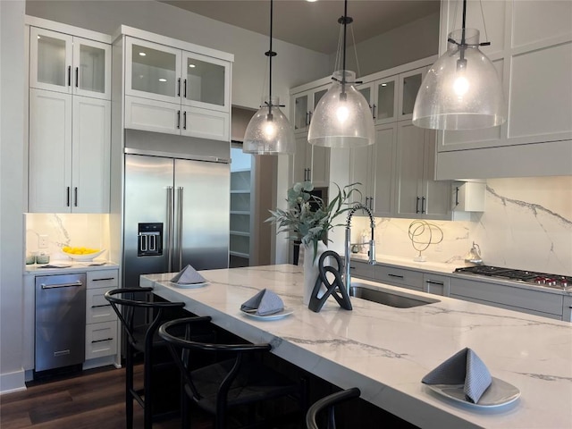 kitchen featuring hanging light fixtures, light stone counters, sink, and stainless steel appliances