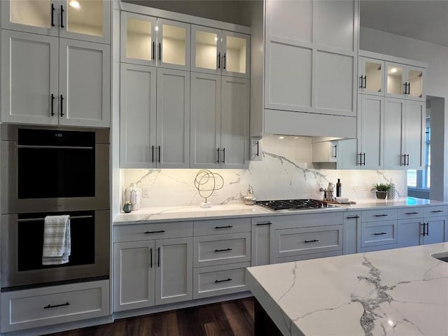 kitchen with white cabinets, decorative backsplash, light stone counters, and stainless steel appliances