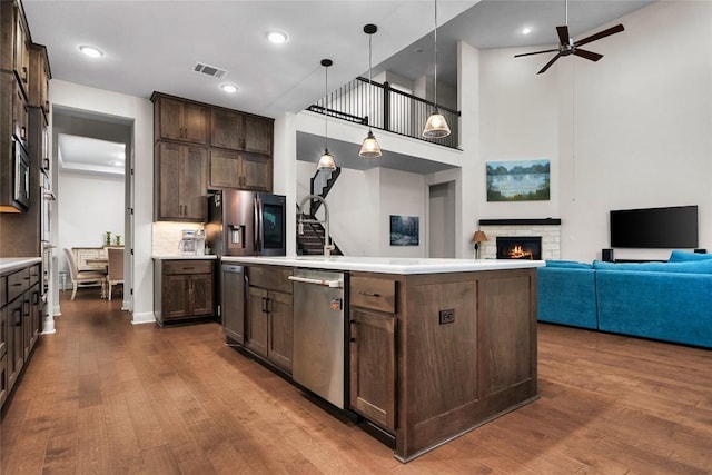 kitchen featuring appliances with stainless steel finishes, dark brown cabinets, pendant lighting, wood-type flooring, and a center island