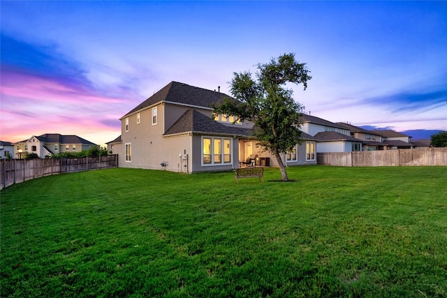 back house at dusk featuring a lawn