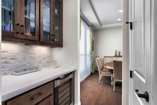 bar with dark brown cabinets, light stone countertops, dark wood-type flooring, and beverage cooler