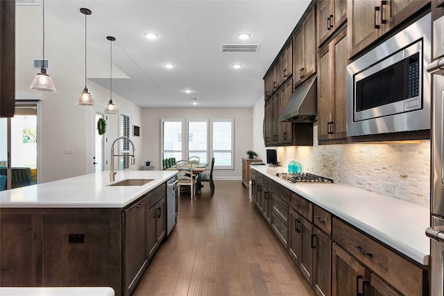 kitchen featuring sink, tasteful backsplash, decorative light fixtures, a center island with sink, and appliances with stainless steel finishes