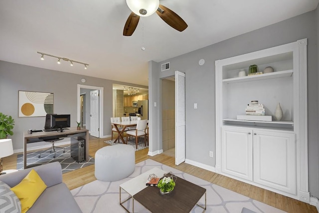 living room with built in shelves, light hardwood / wood-style floors, and ceiling fan