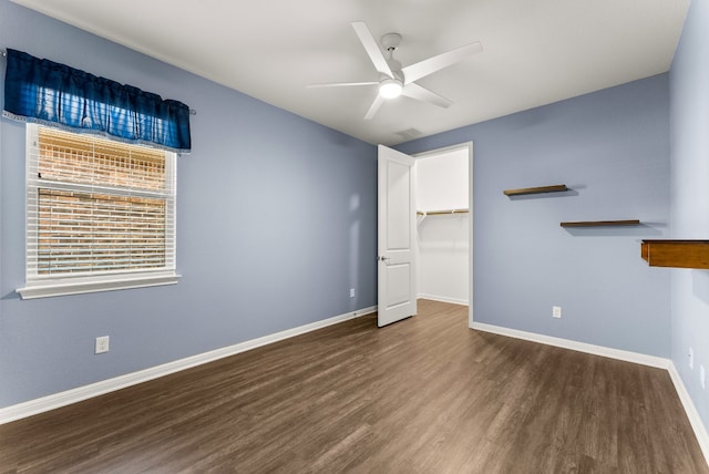 unfurnished bedroom with ceiling fan, a closet, a spacious closet, and dark hardwood / wood-style floors